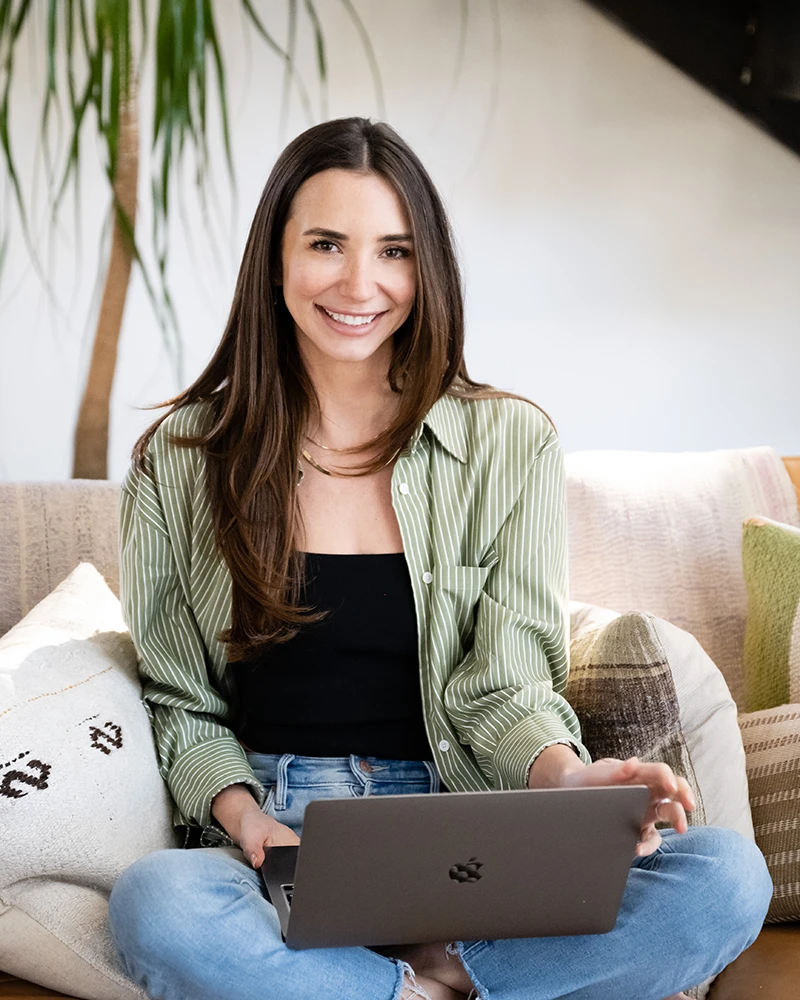 Blaine smiling on a couch, with her laptop