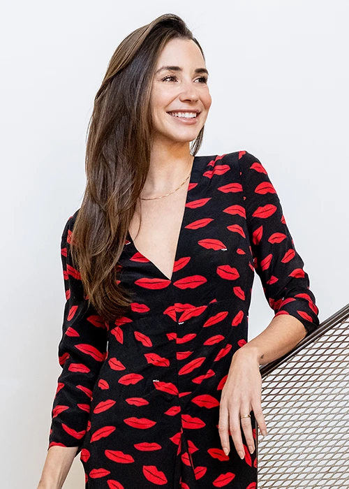 Blaine in a black dress with a red print standing on a staircase, smiling