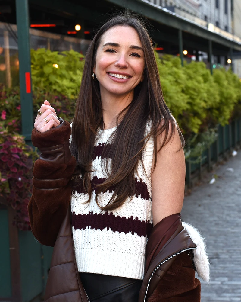 Photo of Blaine on a cobblestone street in Lower Manhattan, with one hand raised, softly smiling